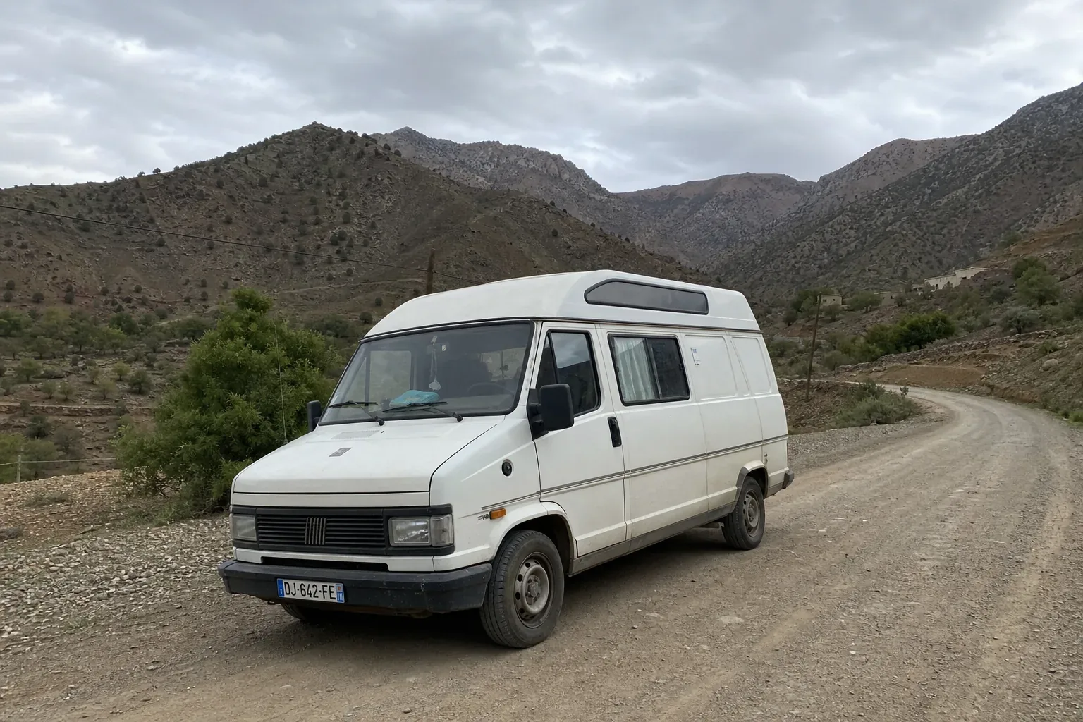 Camping-car d'occasion sur une route rurale du Maroc avec l'Atlas en arrière-plan