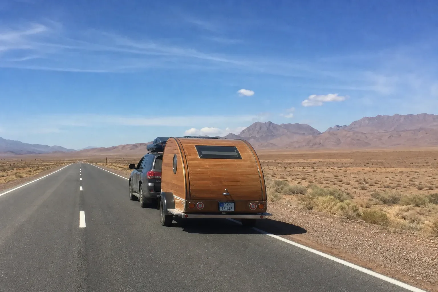 Caravane teardrop tractée par un SUV sur une route ouverte du désert marocain